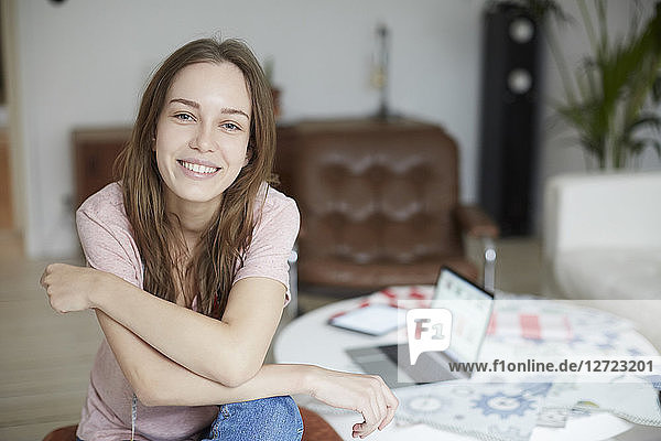 Portrait of smiling fashion designer sitting by table at home