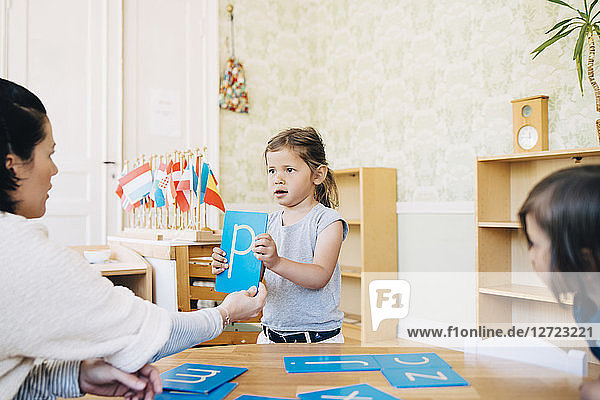 Teacher looking at girl holding letter P in classroom