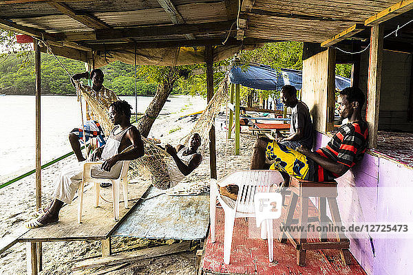 Junge Leute sitzen unter einer Hütte und schauen auf das Meer  Chatham Bay  Union  St-Vincent  St. Vincent und die Grenadinen  Kleine Antillen  Westindische Inseln  Inseln über dem Winde  Karibik  Mittelamerika