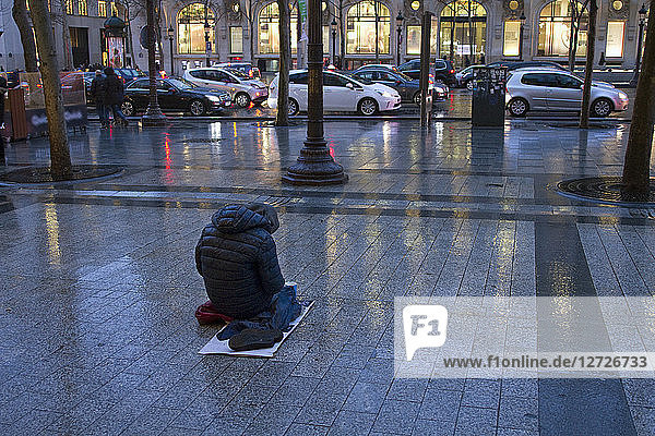 France Paris Avenue des Champs-Elysees a beggar in the rain.