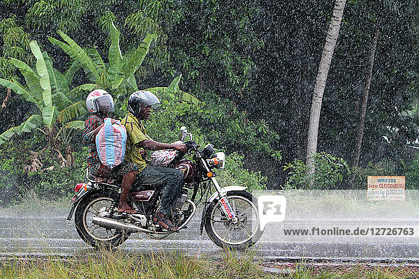 Couple Beninese bikers traveling by motorcycle in the rain. Ouidah. Benin.