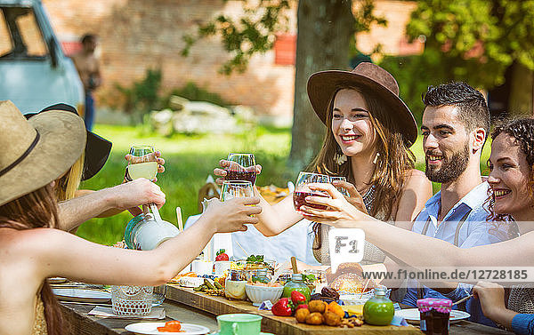 Plan tight of a group of young people seated at a brunch in the country raise their glasses. Mandatory credit: Design culinaire : food-design-studio.fr