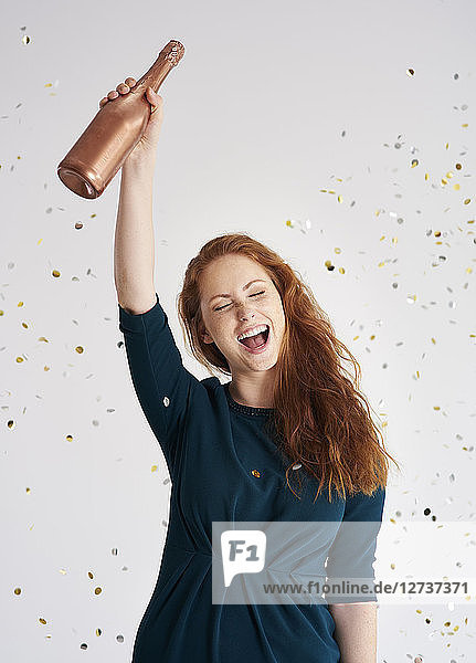 Portrait of happy young woman with bottle of champagne at shower of confetti