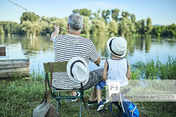 Back view of grandfather and grandson fishing at lakeshore