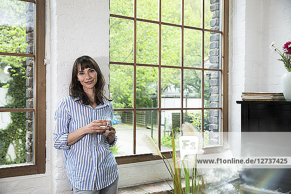 Woman standing at window of her loft apartment  drinking coffee