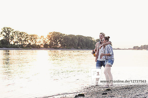 Young couple wading in river at sunset