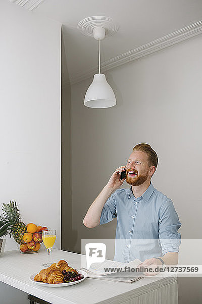 Laughing businessman on the phone at breakfast table at home
