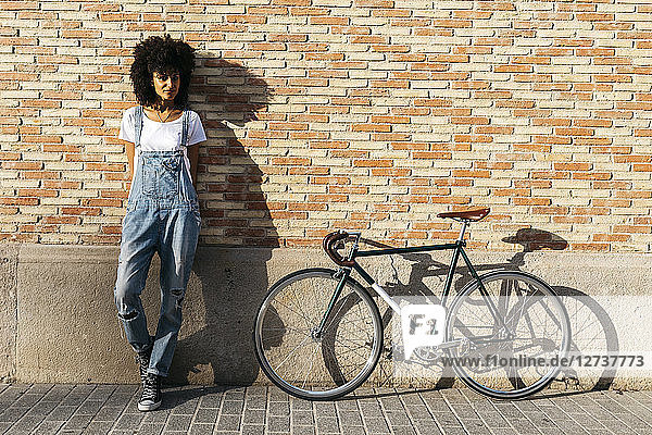 Woman with racing cycle leaning against brick wall