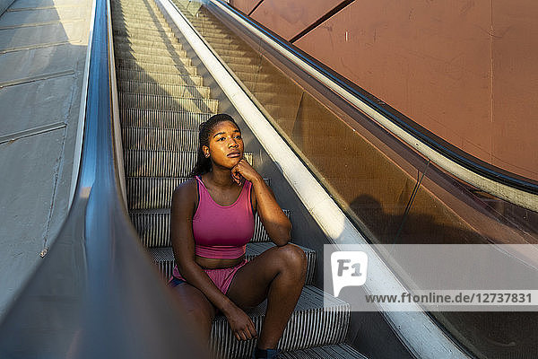 Young sportive woman sitting on escalator