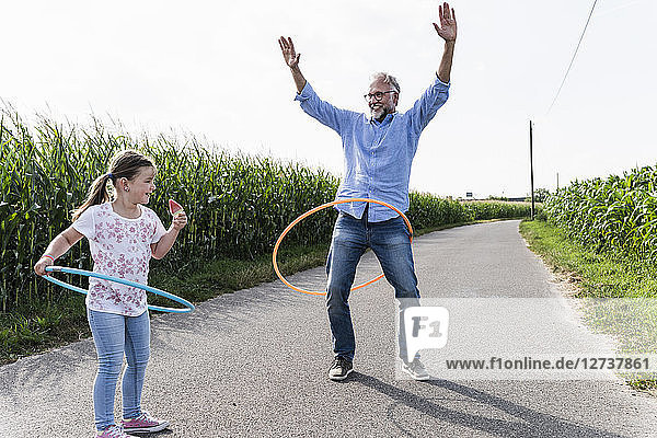 Grandfather and granddaughter playing with hoola hoop in the street