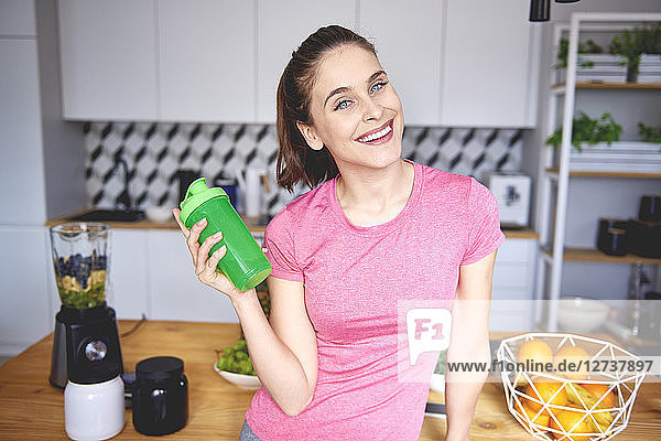 Portrait of smiling young woman with plastic cup preparing smoothie in the kitchen