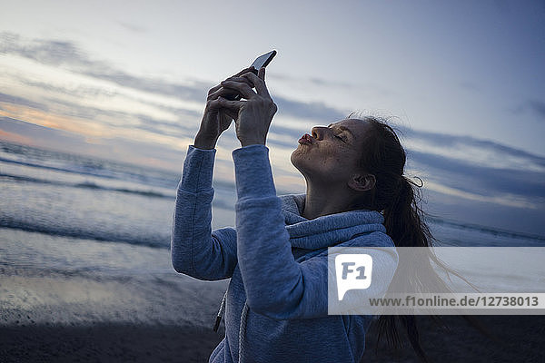 Woman using smartphone on the beach at sunset  sending kiss