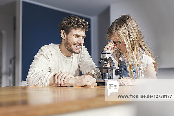 Father watching daughter use a microscope  smiling proudly