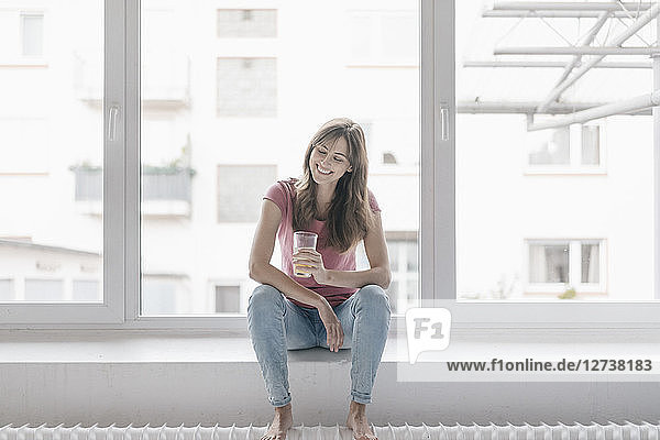 Woman sitting on window sill  holding a glass