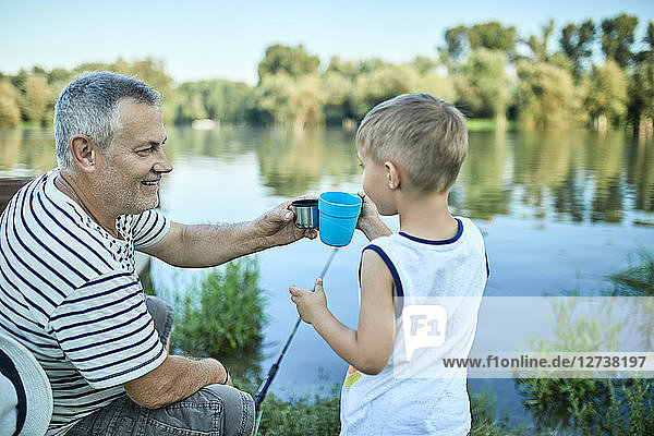 Grandfather and grandson toasting together at lakeshore