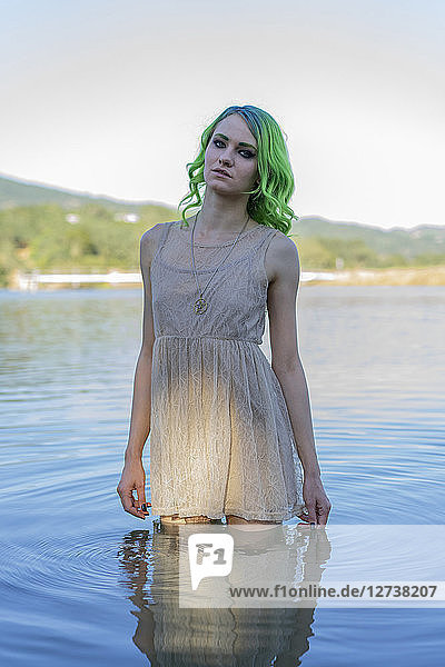 Portrait of young woman with dyed green hair standing dressed in water of lake