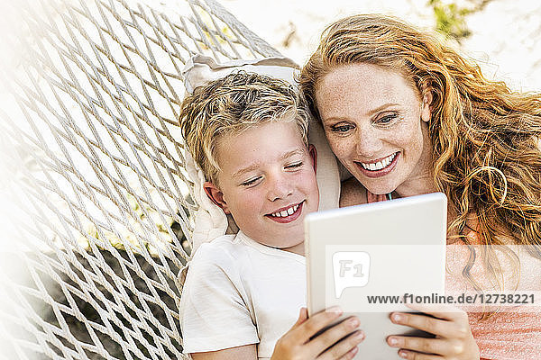 Happy mother and son lying in hammock looking at tablet