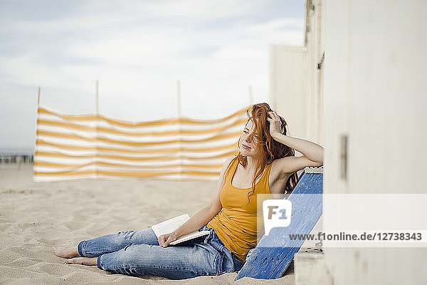 Redheaded woman sitting in front of beach cabin  reading a book