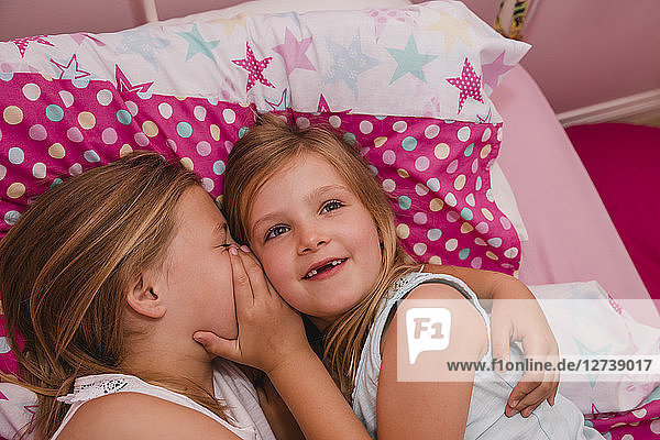 Girl lying on bed with her little sister telling a secret