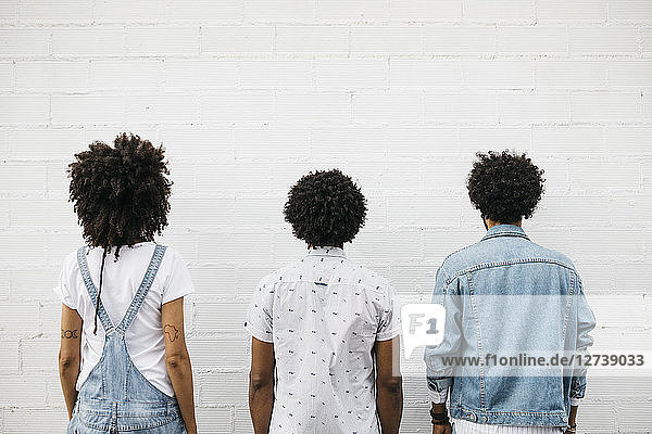 Back view of three friends with curly hair in front of white wall