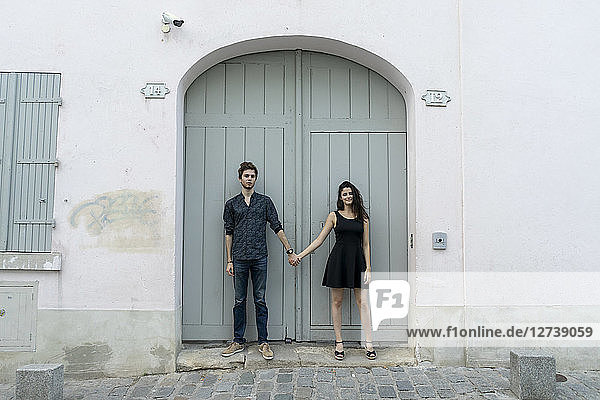 Young couple standing hand in hand in front of building