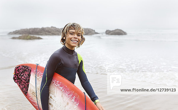Spain  Aviles  portrait of smiling young surfer carrying surfboard on the beach