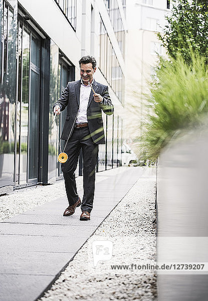 Smiling businessman walking outside office building playing with diabolo