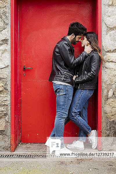 Affectionate young couple kissing at red door