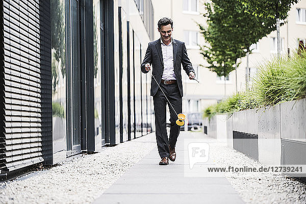 Smiling businessman walking outside office building playing with diabolo