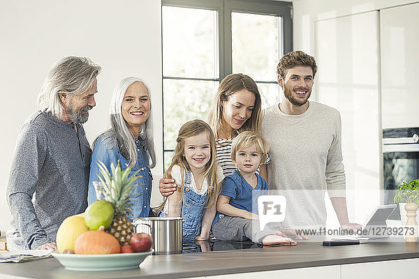 Happy family with grandparents and children standing in the kitchen