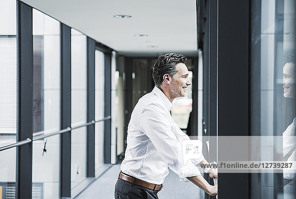 Smiling businessman looking out of window in office passageway