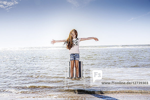 Netherlands  Zandvoort  girl standing on chair in the sea with outstretched arms