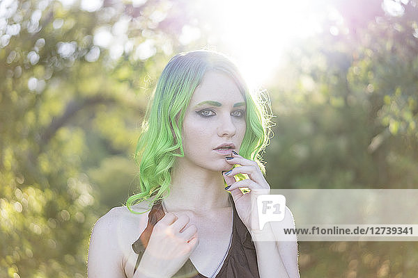 Portrait of young woman with dyed green hair and eyebrows at backlight