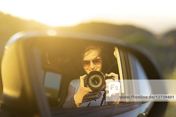 Young woman taking picture of her mirror image in her car