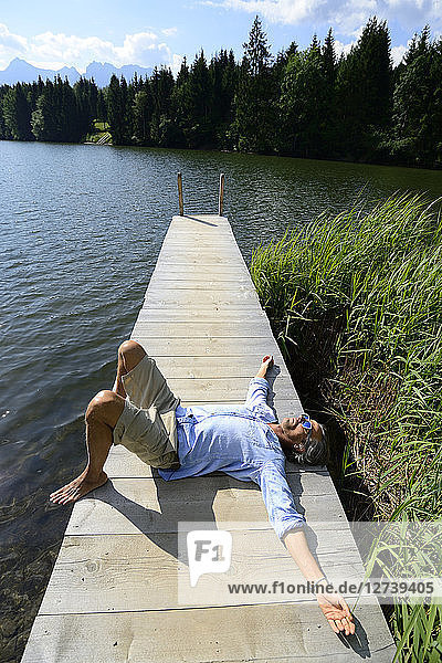 Germany  Mittenwald  mature man lying on jetty at lake relaxing