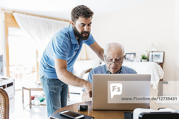 Adult grandson teaching his grandfather to use laptop