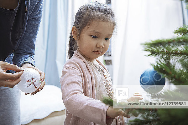 Portrait of little girl decorating Christmas tree with her mother