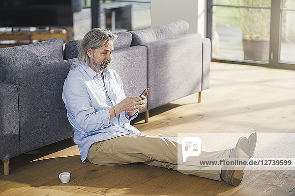 Senior man using smartphone  sitting on floor