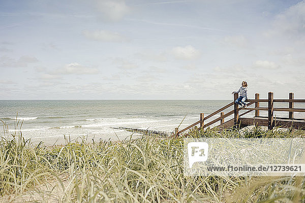 Woman sitting on fence at the beach  relaxing at the sea