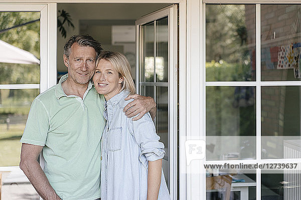 Portrait of smiling mature couple at French window