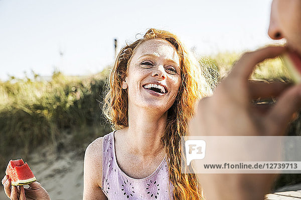 Netherlands  Zandvoort  happy woman eating watermelon looking at man on the beach