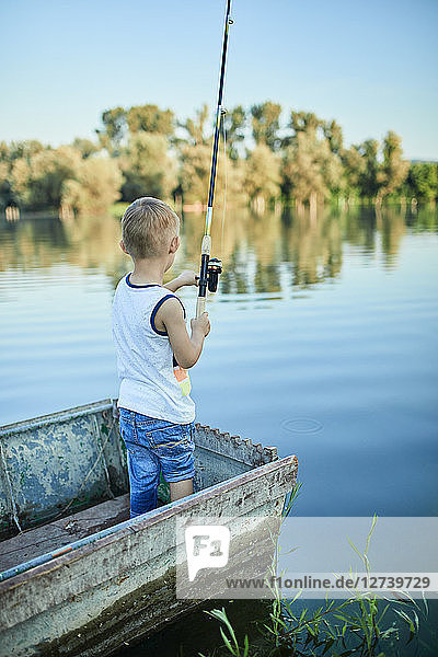 Back view of little boy with fishing rod standing in boat