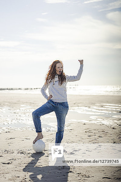 Happy woman having fun at the beach  flexing muscles  playing with soccer ball