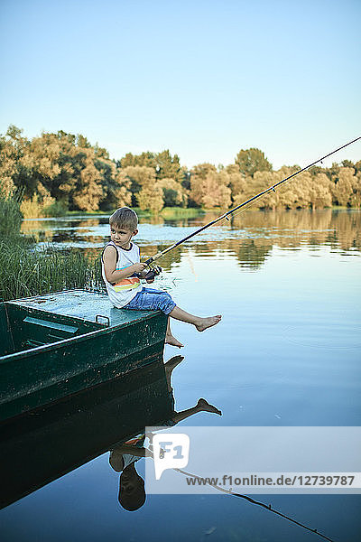 Little boy with fishing rod sitting on boat