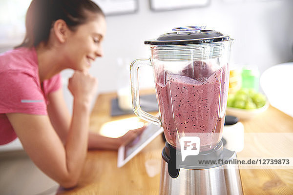 Young woman using tablet in the kitchen while preparing smoothie