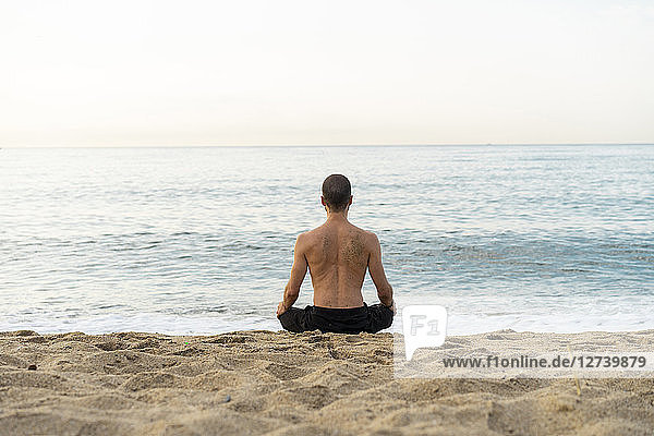 Spain. Man doing yoga on the beach in the evening  meditation  rear view