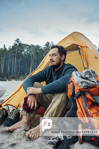 Backpacker sitting in front of his tent on the beach