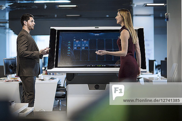 Businesswoman with colleague standing by control screen