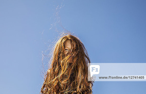 Long red hair covering face of a girl under blue sky
