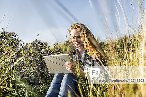 Netherlands  Zandvoort  smiling woman sitting in dunes with tablet